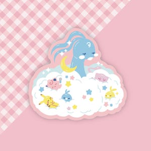 May include: A die-cut sticker featuring a blue cartoon creature with long hair, a yellow crescent moon, and several other cartoon characters in a cloud. The sticker has a pink border and is set against a pink and checkered background.