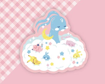 Peut inclure: Un autocollant découpé représentant une créature de dessin animé bleue avec de longs cheveux, un croissant de lune jaune et plusieurs autres personnages de dessins animés dans un nuage. L'autocollant a une bordure rose et est placé sur un fond rose et à carreaux.