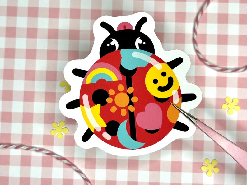 May include: A red ladybug sticker with a black outline and various colorful patterns on its back, including a rainbow, a sun, a heart, a star, and a crescent moon.