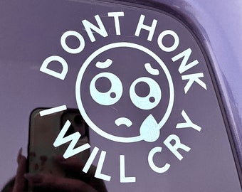 May include: White vinyl sticker with a cartoon face and the text "Don't Honk I Will Cry" on a dark purple car window.