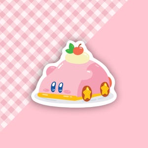 May include: A pink sticker featuring a cartoon character designed as a cake with a cherry on top. The character has blue eyes and star-shaped wheels. The background is a pink and white checkered pattern.