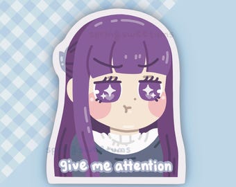Peut inclure: Un autocollant représentant un personnage de style anime avec de longs cheveux violets et des yeux étincelants. Le personnage a un teint pâle et des joues roses. Le texte "give me attention" est en bas. Le fond est bleu clair avec un motif à carreaux.