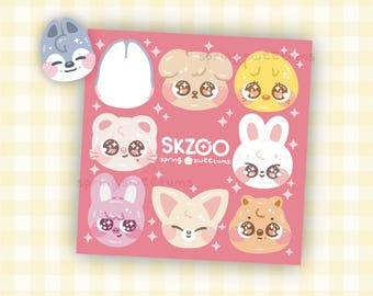Peut inclure: Une planche d'autocollants carrée sur fond rose présentant huit visages d'animaux de dessin animé aux yeux scintillants avec le texte SKZOO spring sweetums, accompagnée d'un autocollant séparé en forme de tête de loup gris.