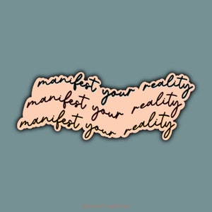 May include: A peach-colored sticker with the text "manifest your reality" repeated three times in black cursive lettering.