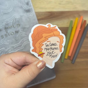 May include: A sticker with a cartoon illustration of a woman with orange hair and a planet around her neck. The sticker has the text "Take chances, make mistakes, get messy".