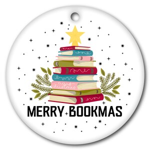 Peut inclure: Ornement de Noël rond blanc avec une pile de livres en forme d'arbre, surmontée d'une étoile dorée. L'ornement porte l'inscription "MERRY + BOOKMAS" en noir, avec de petites étoiles dispersées autour du motif.