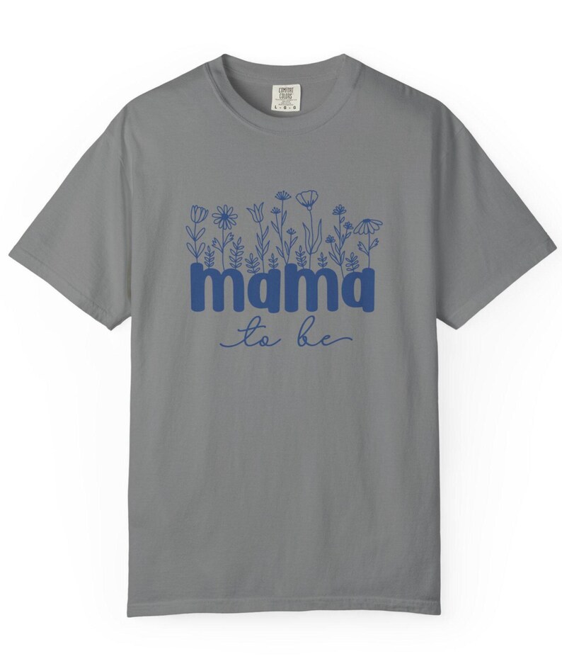 May include: Gray t-shirt with the words "mama to be" in blue, with a floral design above the word "mama". The shirt is a crew neck and has short sleeves. The text is in a script font.