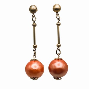 May include: A pair of gold tone dangle earrings with large orange round beads.