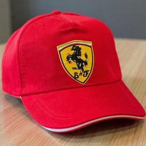 May include: A vibrant red baseball cap with the Ferrari emblem. The logo is a black prancing horse on a yellow shield with green, white, and red stripes. The cap has a white and red trim on the peak.