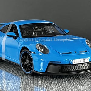 May include: A bright blue sports car model with black wheels and trim. The car has a rear spoiler and a white stripe. The number plate displays 'S. GT 3992'.