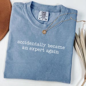 Op de afbeelding: Een witte keramische mok met een zwarte handgreep en de tekst "But First, Coffee" in een vetgedrukte, zwarte letter. De mok staat tegen een vage achtergrond, wat het strakke ontwerp benadrukt.