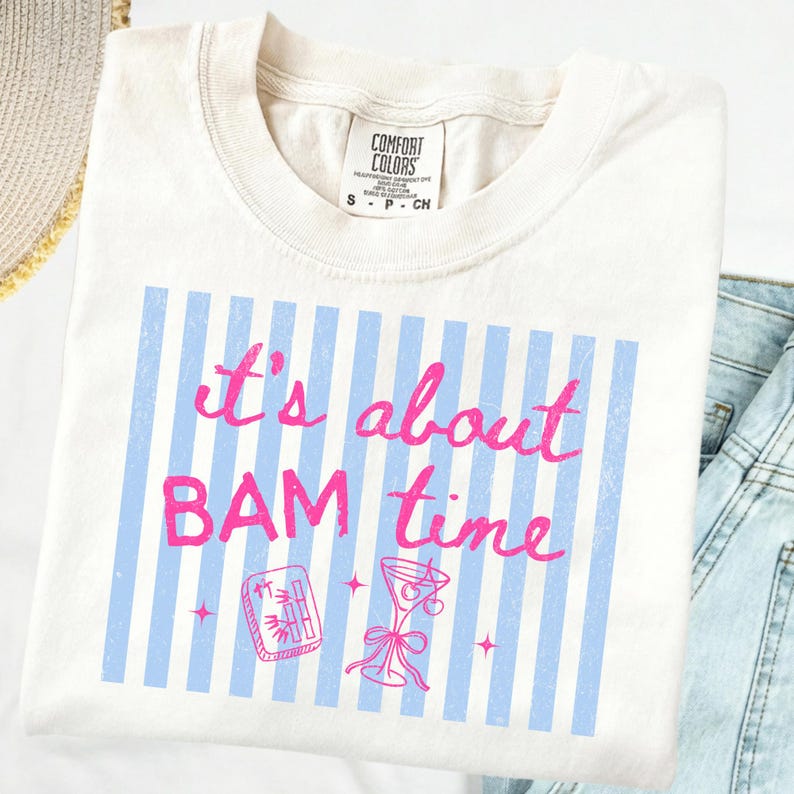 Puede incluir: Camiseta color crema con la frase "It's about BAM time" en rosa sobre rayas verticales azul claro. El dise&ntilde;o incluye un c&oacute;ctel y una ilustraci&oacute;n de ficha de mahjong.