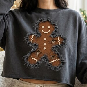 Peut inclure: Un sweat-shirt gris anthracite à col rond orné d'une applique en forme de bonhomme en pain d'épice marron aux bords effilochés. Le bonhomme présente un sourire brodé blanc, trois boutons blancs et des empiècements léopard.