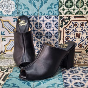 May include: A pair of black leather peep-toe heeled clogs with a block heel. The clogs have a gold label on the inside that says "Vintage Esprite".
