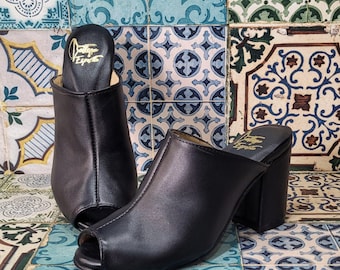 Puede incluir: Un par de zuecos de tacón negro de cuero con puntera abierta. Los zuecos tienen una etiqueta dorada en el interior que dice "Vintage Esprite".