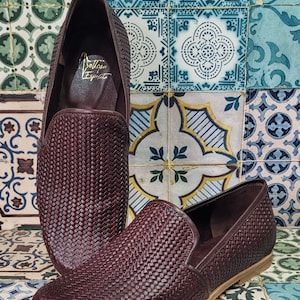 May include: A pair of dark brown woven leather loafers with a brown leather sole. The loafers have a woven pattern and the text "Dolce & Esprite" is visible on the inside of one of the loafers.