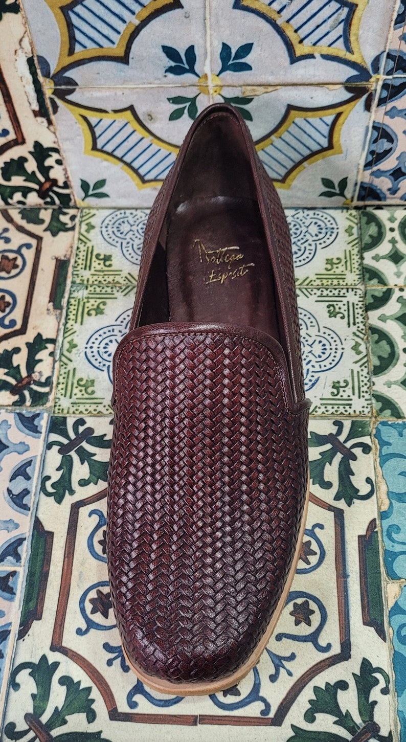 May include: A pair of brown leather woven slip-on shoes with a rounded toe. The shoes have a woven leather upper and a leather sole. The brand name "Soltana Espirit" is written on the inside of the shoe.