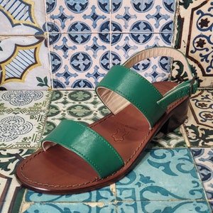 May include: Green leather heeled sandals with two straps and a brown leather sole. The sandals are on a patterned tile background.