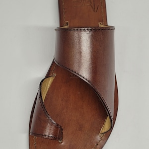 May include: Brown leather sandals with a strap that wraps around the ankle. The sandals have a simple design and are made of high-quality leather.