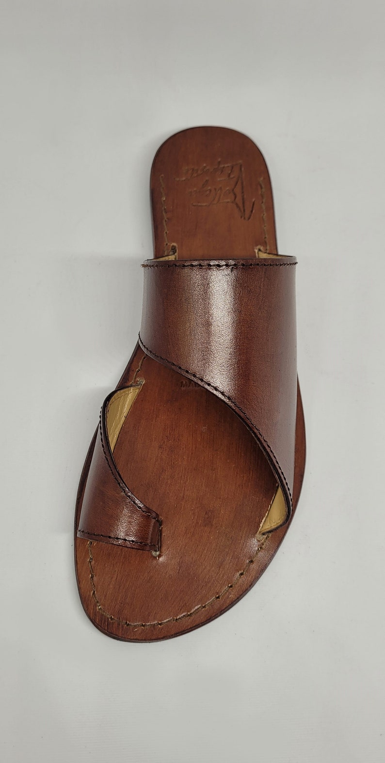 May include: Brown leather sandals with a strap that wraps around the ankle. The sandals have a simple design and are made of high-quality leather.