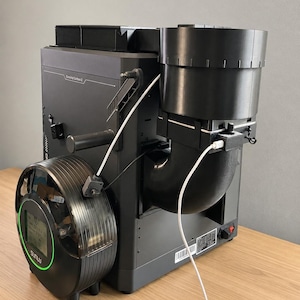 Może przedstawiać: Czarne akcesorium do drukarki 3D z etykietą Creality Carbon 2, okrągłą suszarką do filamentu Sunlu z zielonym pierścieniem LED oraz dużym czarnym cylindrycznym kanałem wylotowym połączonym białymi kablami zasilającymi z obudową.