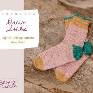 Peut inclure: Une paire de chaussettes en tricot rose et jaune avec un talon et une pointe verts. Les chaussettes sont sur une surface rocheuse. Le texte "Dawn Socks" et "téléchargement de modèle de tricot numérique" est sur un fond blanc.