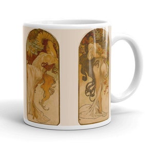 Könnte beinhalten: Weiße Keramiktasse mit zwei Jugendstil-Illustrationen von Frauen mit fließendem Haar und floralen Elementen in Beige, Gold und Rot. Die Tasse hat einen gebogenen Henkel.