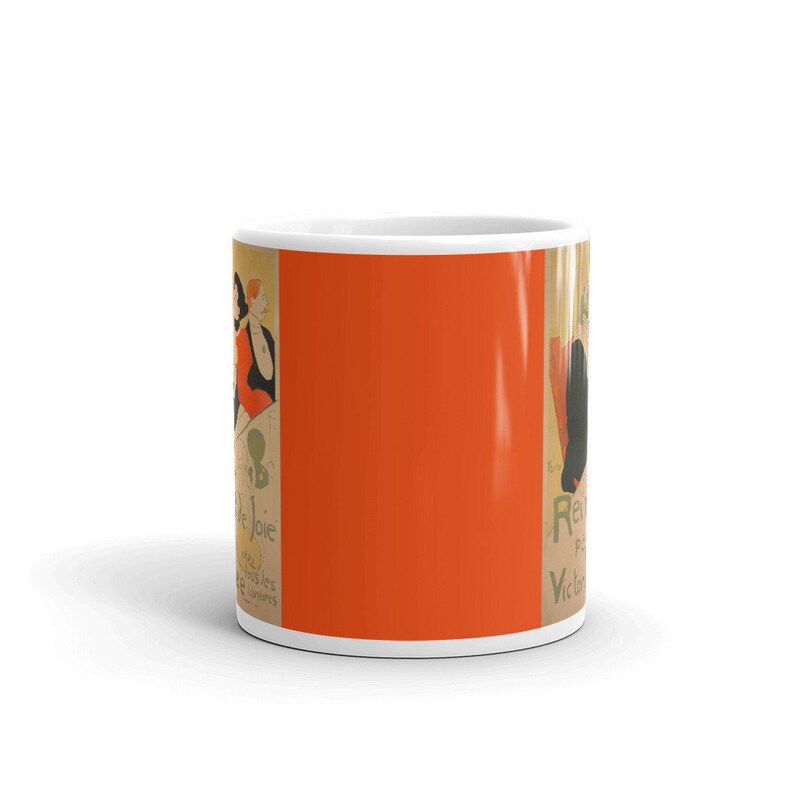 May include: A white ceramic mug with a vintage poster design featuring a woman in a red dress and the text "Revue de Joie" in green and black. The background is orange.