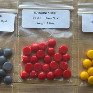 May include: Three small plastic bags each containing colorful glass beads. The bags are labeled "JCAROLINE STUDIO" with the bead type and weight. The beads are gray, red, and yellow. Each bag weighs 1.0 oz.