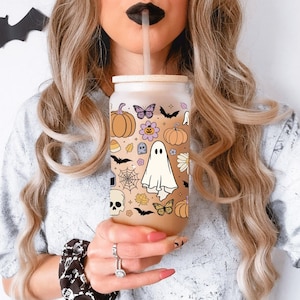 Pu&ograve; includere: Un bicchiere di vetro smerigliato a forma di lattina con un design a tema Halloween. Il design include zucche, farfalle, pipistrelli, un fantasma e una ragnatela. Il bicchiere ha un coperchio di bamb&ugrave; e una cannuccia.