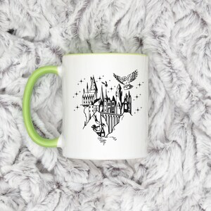 Puede incluir: Taza de cer&aacute;mica blanca con asa y borde verdes. La taza presenta una ilustraci&oacute;n negra de un castillo, un b&uacute;ho que lleva una carta y estrellas. El dise&ntilde;o recuerda un tema de fantas&iacute;a.
