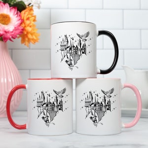 Puede incluir: Tres tazas de cer&aacute;mica blancas con detalles en negro, rojo y rosa. Cada taza presenta una ilustraci&oacute;n negra de un castillo, un b&uacute;ho y estrellas. Las tazas est&aacute;n apiladas, con un jarr&oacute;n de flores en el fondo.