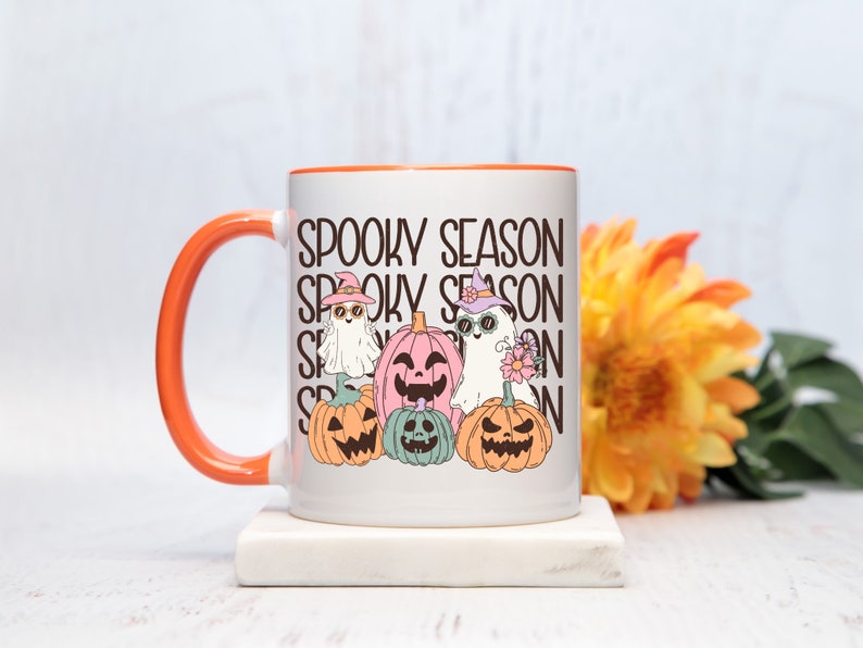 May include: White ceramic mug with an orange handle and rim, featuring a "Spooky Season" design. The design includes cartoon ghosts and jack-o'-lanterns in pastel colors. A perfect gift for Halloween lovers.