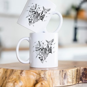 Puede incluir: Dos tazas de cer&aacute;mica blanca con una ilustraci&oacute;n negra de un castillo, un b&uacute;ho y estrellas. Las tazas est&aacute;n apiladas sobre una superficie de madera. El dise&ntilde;o tiene un tema de fantas&iacute;a.