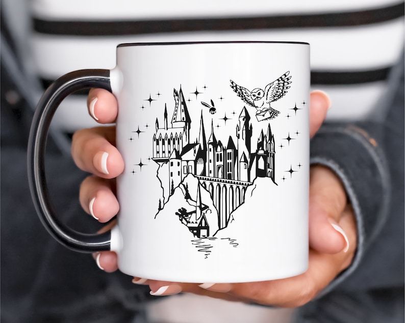 Puede incluir: Taza de cer&aacute;mica blanca con interior y asa negros. La taza presenta una ilustraci&oacute;n negra de un castillo, un b&uacute;ho que lleva una carta y estrellas. El dise&ntilde;o evoca un tema de fantas&iacute;a.