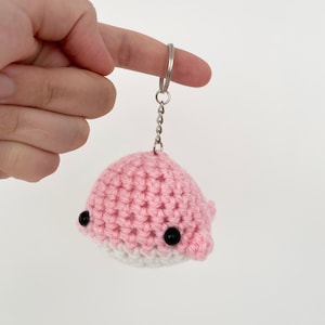May include: A pink and white crocheted whale keychain with black eyes.