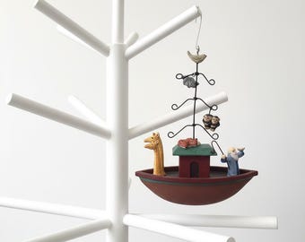 May include: A white coat rack with multiple arms, holding a decorative ornament. The ornament features a boat with figurines of a giraffe, a man, and a house. Above the boat is a wire structure with animal figurines.
