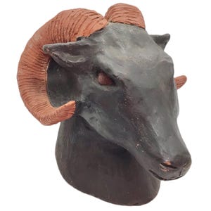 May include: A black ceramic ram head sculpture with large, curled, terracotta horns.