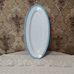 May include: A white oval serving platter with a light blue rim. The platter is on a white crocheted tablecloth.