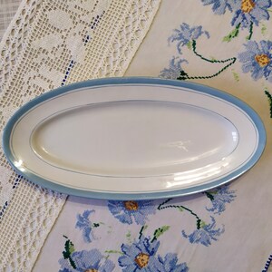 May include: A white oval serving platter with a light blue rim and two thin blue lines around the edge.
