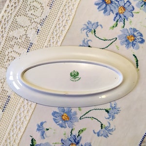 May include: White oval serving platter with a green and gold emblem on the bottom. The emblem features a double-headed eagle and the text "Фабрика" in Cyrillic.