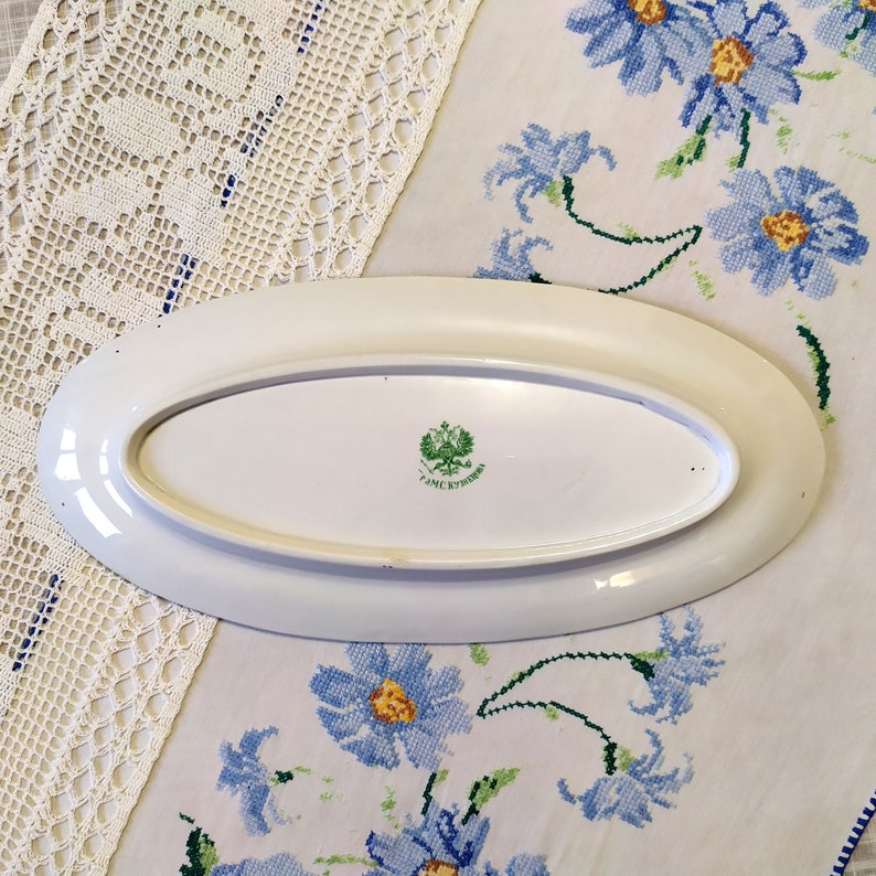May include: White oval serving platter with a green and gold emblem on the bottom. The emblem features a double-headed eagle and the text "Фабрика" in Cyrillic.