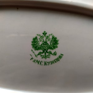 May include: A green and white porcelain plate with a green imperial Russian coat of arms and the text "Г.М.С. Кузнецова" in green.