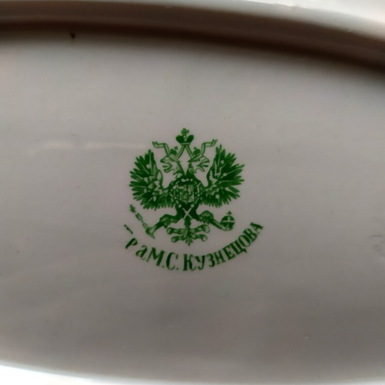 May include: A green and white porcelain plate with a green imperial Russian coat of arms and the text "Г.М.С. Кузнецова" in green.