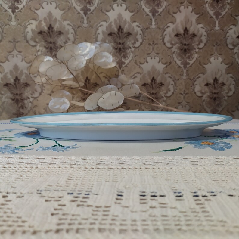 May include: A light blue oval serving platter with a white rim. The platter is sitting on a white crocheted tablecloth.