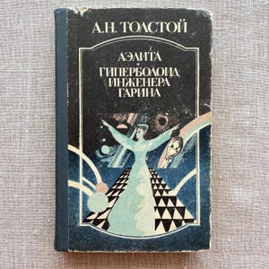 May include: Vintage hardcover book with a dark blue cover featuring the title "A.H. Tolstoy" and a title in Russian. The cover art depicts a woman with outstretched arms against a backdrop of geometric shapes and celestial elements. The book's spine is a darker blue.