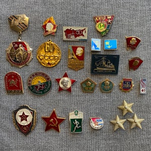 Puede incluir: Una colección de pines de esmalte de la era soviética vintage. Los pines presentan una variedad de diseños, incluyendo estrellas, banderas y figuras políticas. Los pines son de varios colores, incluyendo rojo, azul, amarillo y verde.