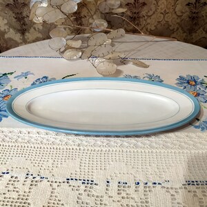 May include: A white oval serving platter with a light blue rim and a thin white stripe around the edge.