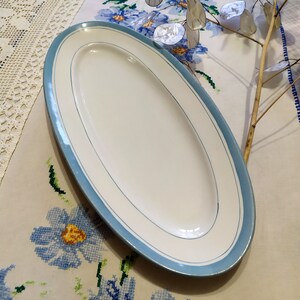 May include: A white oval serving platter with a light blue rim and two thin white lines around the edge.