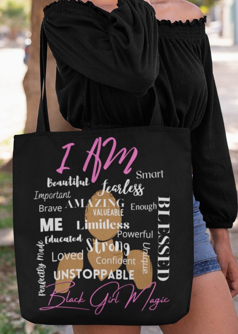 May include: Black tote bag with a pink and brown design. The bag features the text "I AM" in pink and a list of positive affirmations in black and brown. The text "Black Girl Magic" is written in pink at the bottom of the bag.